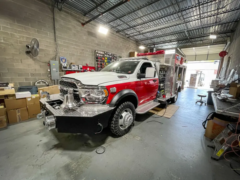 Exterior view of small fire truck showing cab, body compartments, and wheel/tire area.